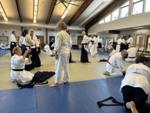 People on aikido mat, some folding hakama pants, and talking